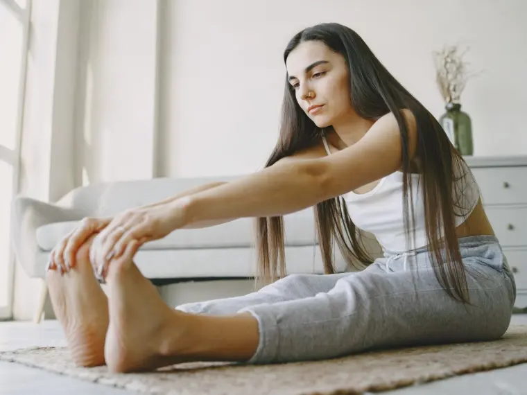 Mulher realizando um alongamento no chão de uma sala clara durante aula de pilates.